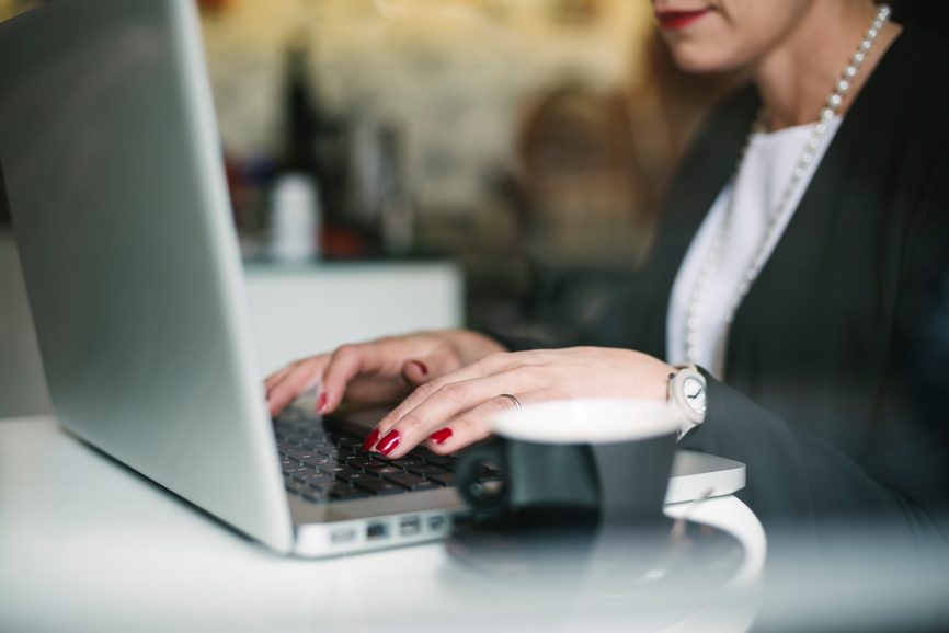 Close up view of woman's hand typing on a laptop with a coffee cup
