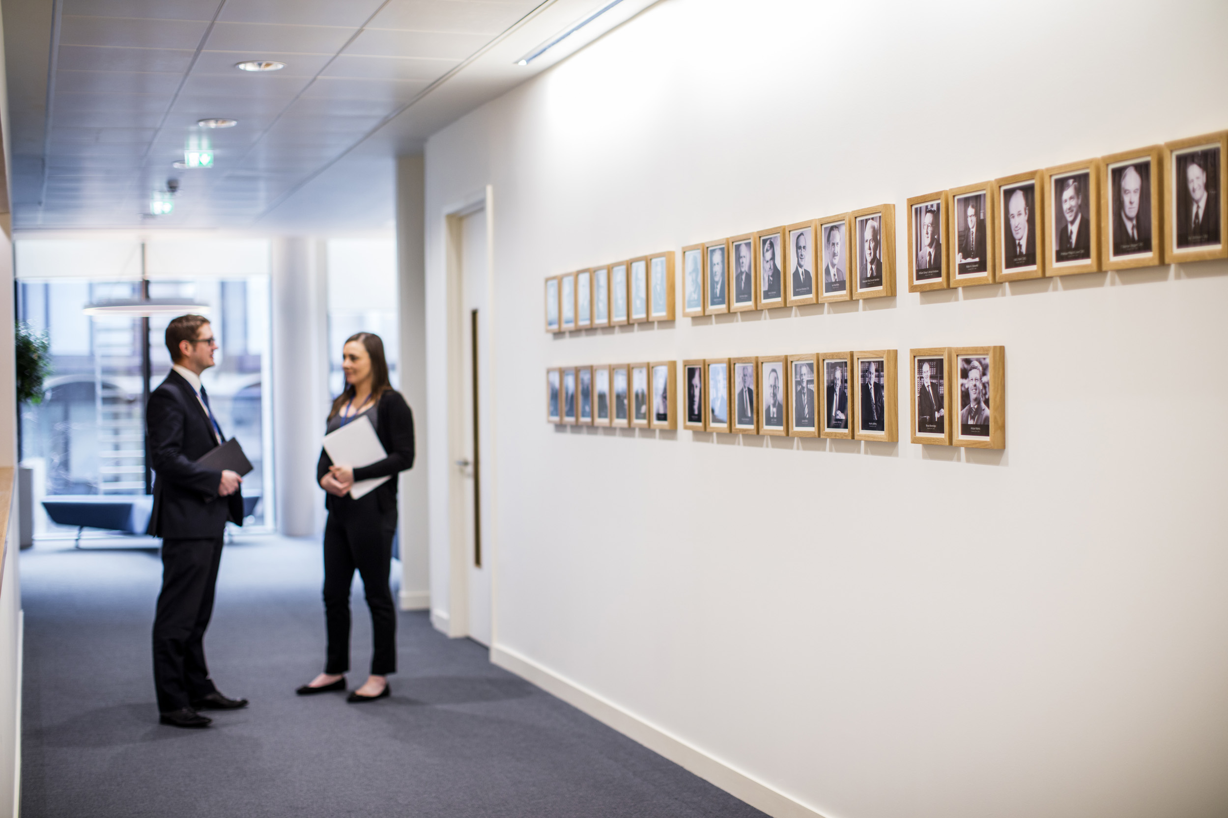 A corridor lined with photographs and two people standing and chatting